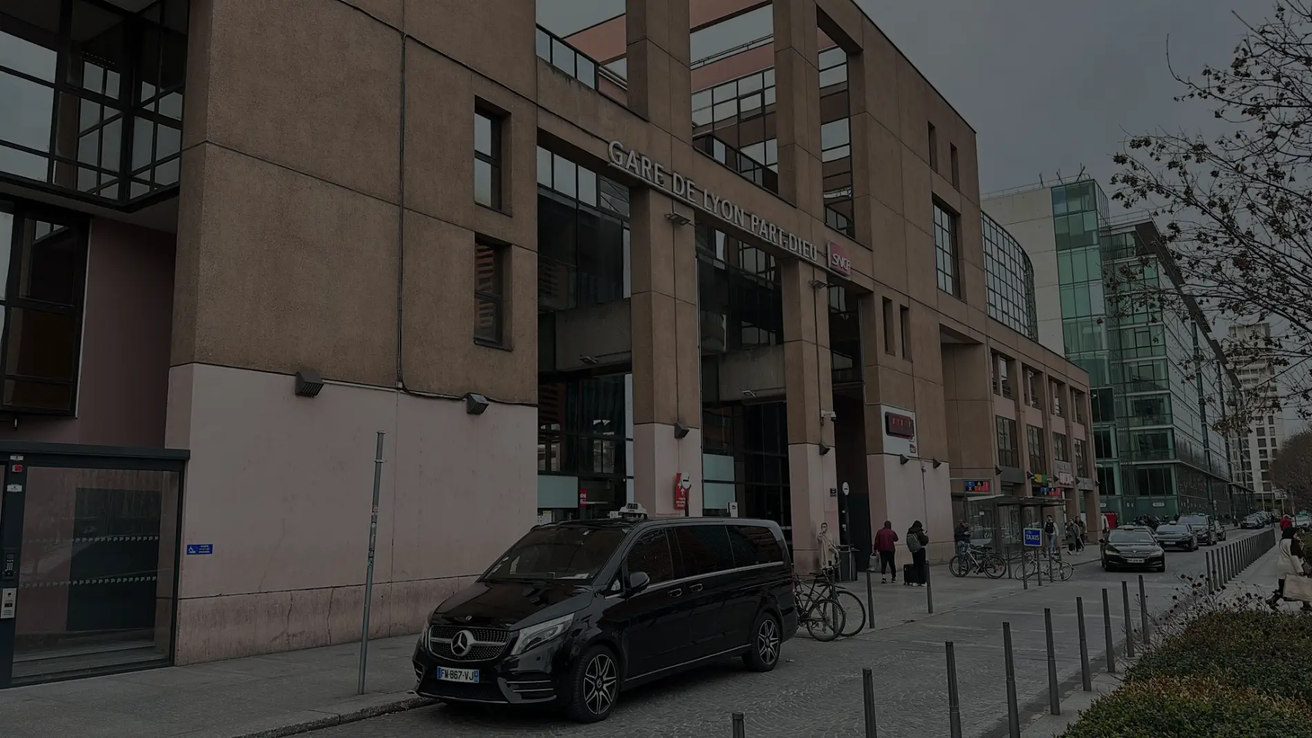 Van Mercedes Classe V noir en stationnement devant l'entrée de la Gare de Lyon Part-Dieu pour un service de taxi et transfert gare.